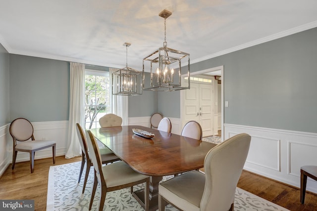 dining space featuring ornamental molding, a notable chandelier, a wainscoted wall, and wood finished floors