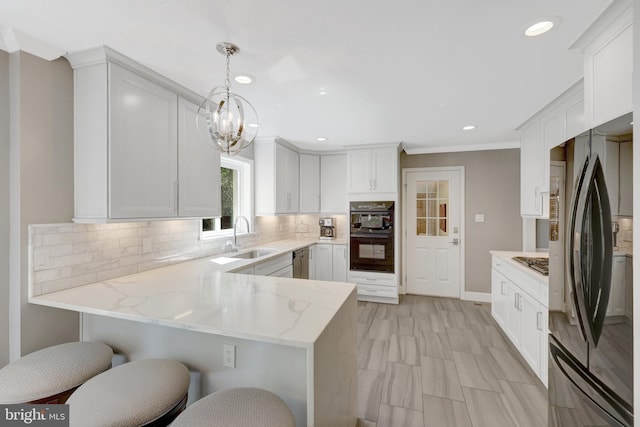 kitchen with a sink, a peninsula, black appliances, white cabinets, and light stone countertops