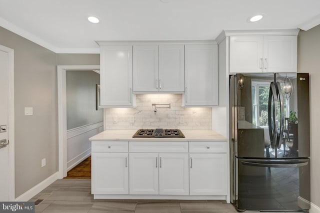 kitchen with stovetop with downdraft, freestanding refrigerator, decorative backsplash, white cabinets, and baseboards