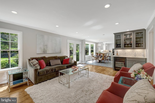 living room with bar, crown molding, light wood-type flooring, wine cooler, and recessed lighting