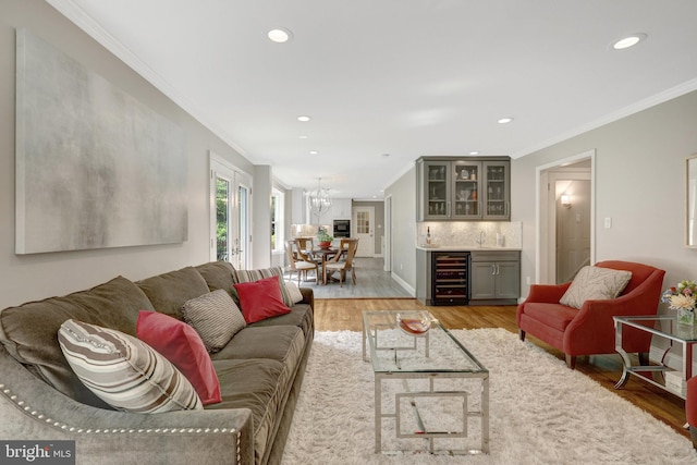 living room with an inviting chandelier, light wood-style flooring, crown molding, a dry bar, and wine cooler