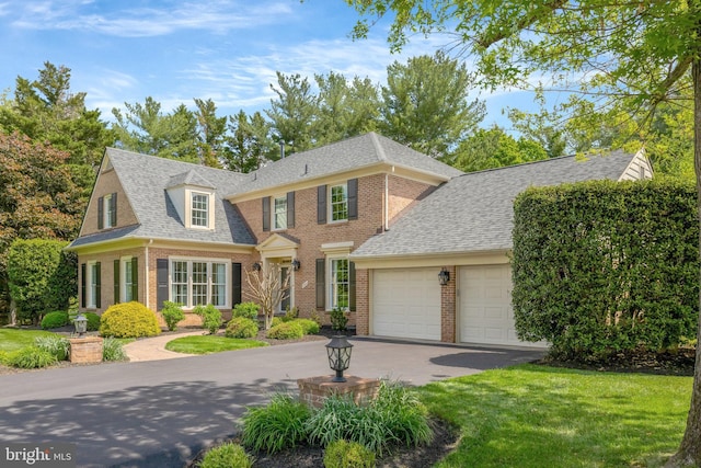 view of front of property featuring an attached garage, aphalt driveway, a shingled roof, a front yard, and brick siding
