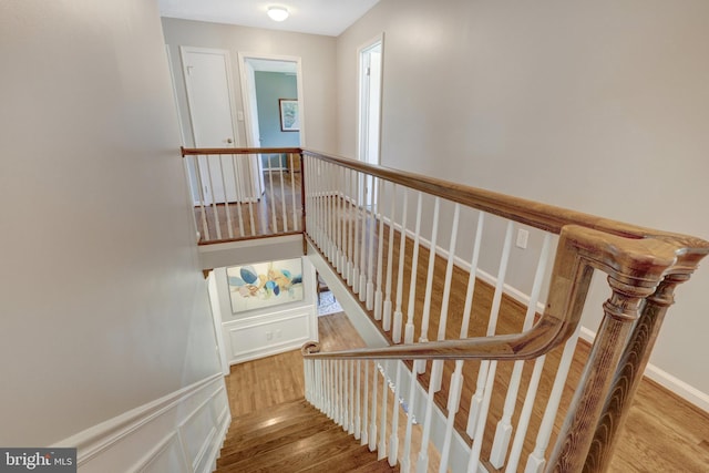 stairs with a decorative wall and wood finished floors