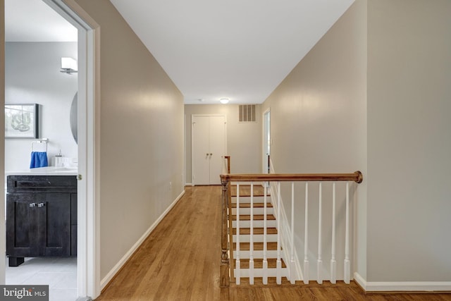 hall with baseboards, light wood-style floors, an upstairs landing, and visible vents