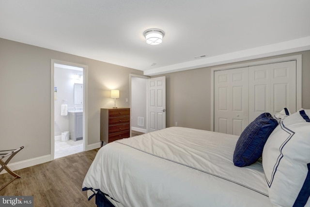 bedroom featuring a closet, baseboards, ensuite bathroom, visible vents, and wood finished floors