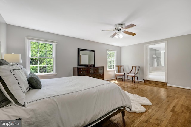 bedroom featuring a ceiling fan, ensuite bath, wood finished floors, and baseboards