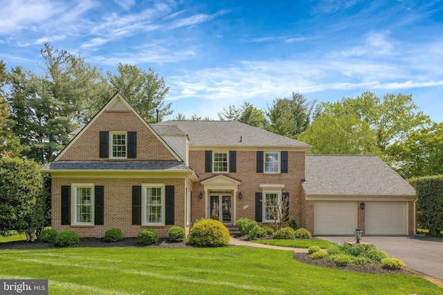 view of front of house featuring roof with shingles, brick siding, driveway, a garage, and a front yard