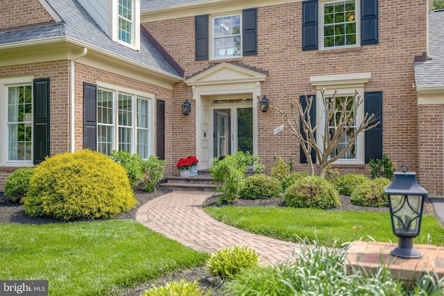 doorway to property featuring roof with shingles and brick siding