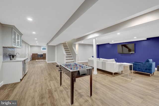 game room with light wood-style flooring, indoor wet bar, a sink, baseboards, and recessed lighting