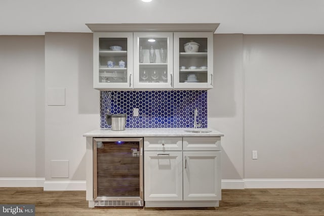 bar with a sink, wood finished floors, baseboards, and beverage cooler