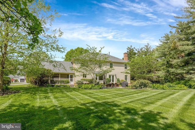 rear view of property with a lawn, a chimney, and a sunroom