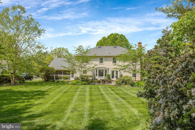 rear view of house featuring a yard, a chimney, and a sunroom