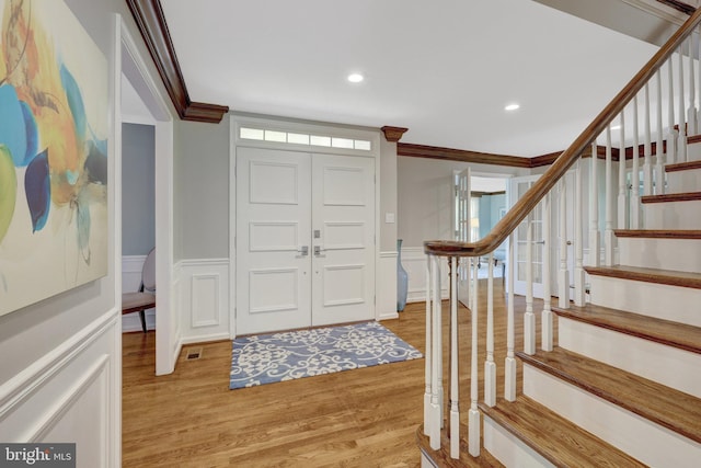 entrance foyer with stairs, wood finished floors, ornamental molding, recessed lighting, and wainscoting