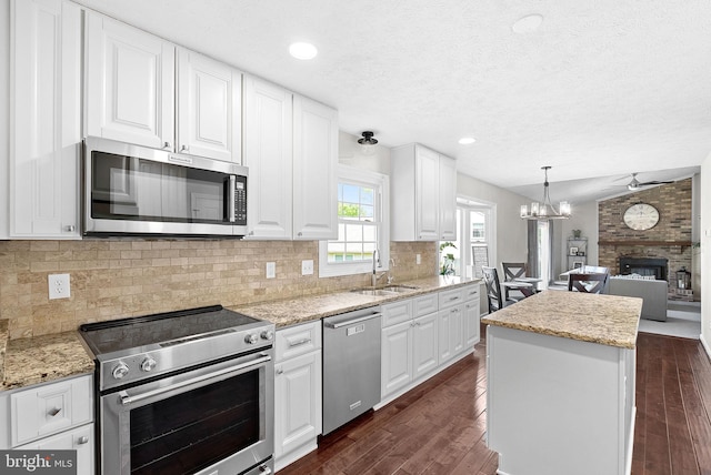 kitchen featuring open floor plan, dark wood-style floors, a large fireplace, a sink, and appliances with stainless steel finishes