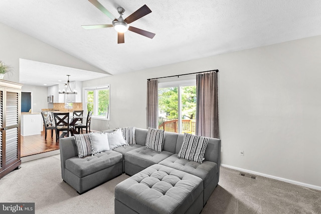 living room featuring vaulted ceiling, light carpet, ceiling fan with notable chandelier, and visible vents