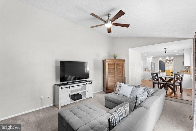 living area with baseboards, vaulted ceiling, light carpet, and ceiling fan with notable chandelier