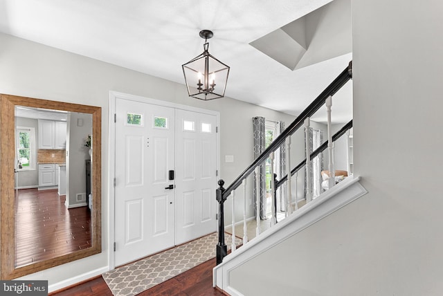 foyer entrance featuring baseboards, dark wood finished floors, stairs, and a notable chandelier