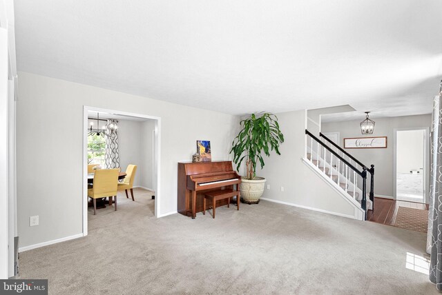 sitting room featuring an inviting chandelier, baseboards, carpet floors, and stairway