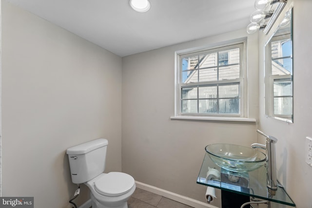half bathroom featuring toilet, tile patterned flooring, baseboards, and a sink