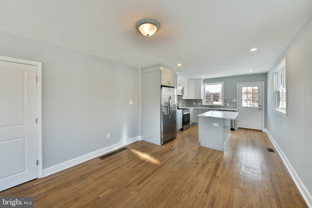 kitchen featuring backsplash, appliances with stainless steel finishes, wood finished floors, light countertops, and baseboards