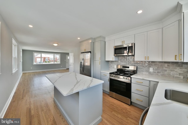 kitchen with light wood finished floors, appliances with stainless steel finishes, a kitchen island, and tasteful backsplash