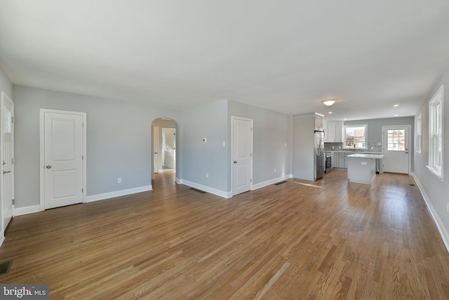 unfurnished living room featuring arched walkways, baseboards, visible vents, and light wood finished floors