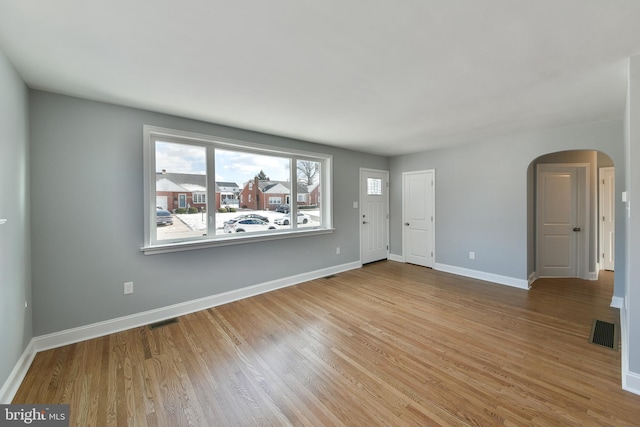 unfurnished living room with arched walkways, visible vents, and wood finished floors