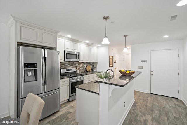 kitchen featuring appliances with stainless steel finishes, a sink, wood finished floors, tasteful backsplash, and visible vents