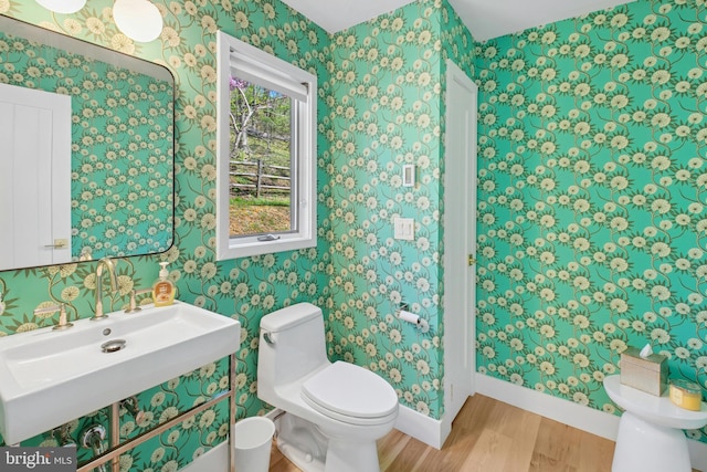 half bathroom with wood finished floors, toilet, baseboards, wallpapered walls, and a sink