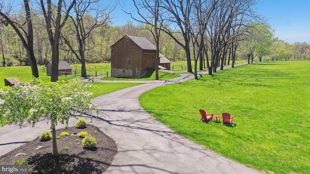 view of property's community featuring a lawn, a barn, fence, and an outbuilding