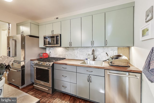 kitchen featuring dark wood-style flooring, appliances with stainless steel finishes, tasteful backsplash, a sink, and wood counters
