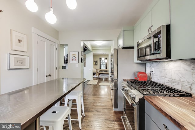 kitchen with decorative backsplash, butcher block counters, a kitchen breakfast bar, dark wood-type flooring, and appliances with stainless steel finishes