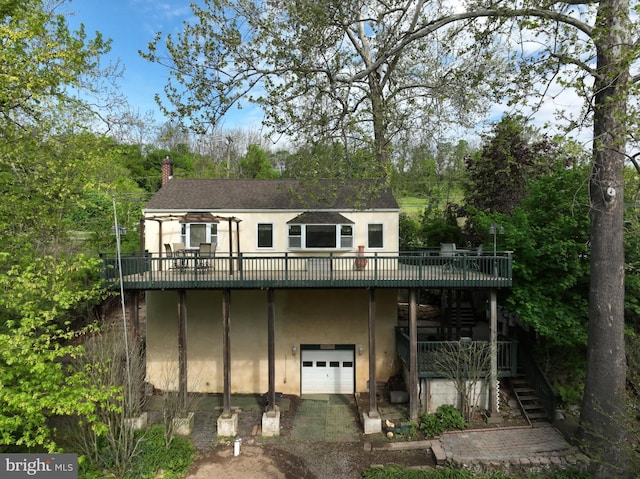 rear view of property with a garage, a wooden deck, stairs, and stucco siding