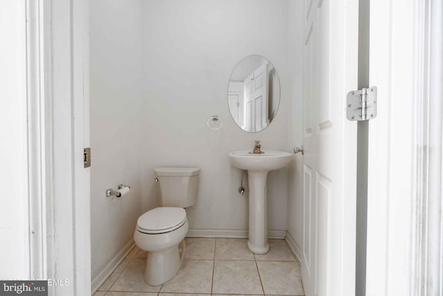 half bathroom with toilet, tile patterned floors, a sink, and baseboards