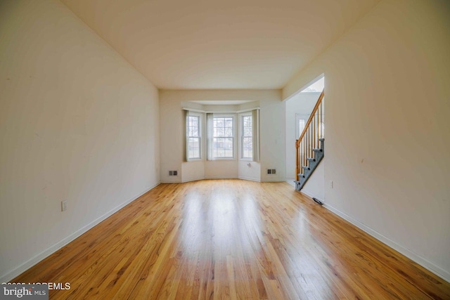 spare room featuring light wood-style floors, stairs, baseboards, and visible vents