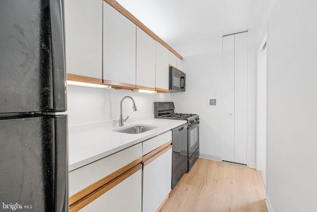 kitchen with light wood-type flooring, light countertops, white cabinets, a sink, and black appliances