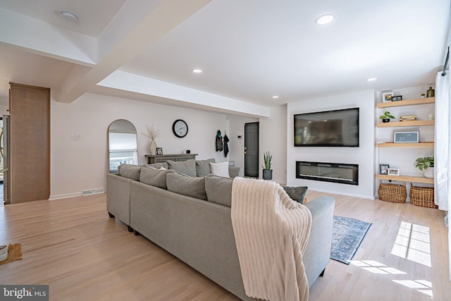 living room featuring a glass covered fireplace, beamed ceiling, light wood-style floors, recessed lighting, and arched walkways