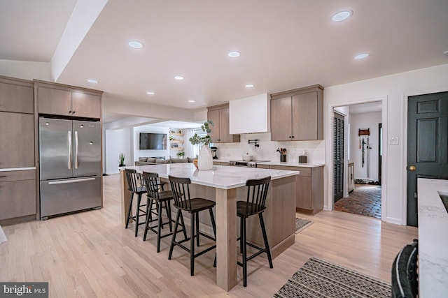 kitchen featuring stainless steel fridge, light countertops, light wood-type flooring, a kitchen bar, and a kitchen island