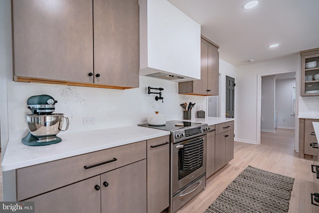 kitchen featuring backsplash, stainless steel electric range, light countertops, ventilation hood, and light wood-style flooring