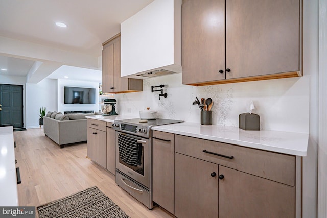 kitchen with tasteful backsplash, light wood-type flooring, stainless steel range with electric cooktop, light countertops, and custom range hood