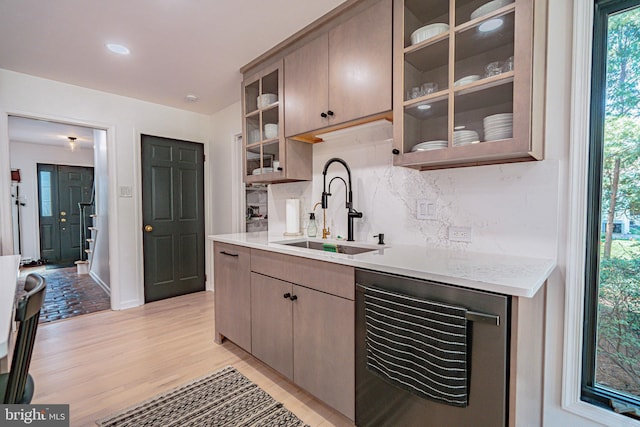 kitchen featuring a sink, light wood finished floors, light countertops, baseboards, and tasteful backsplash