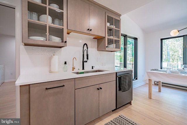 kitchen with a sink, light wood finished floors, decorative backsplash, stainless steel dishwasher, and vaulted ceiling