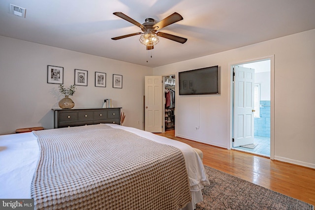 bedroom featuring visible vents, ensuite bath, light wood-style floors, baseboards, and a spacious closet