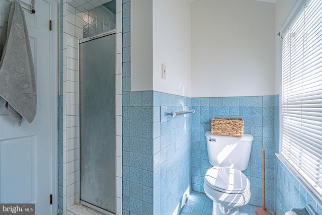 full bath with toilet, tile walls, a wainscoted wall, tile patterned floors, and a stall shower