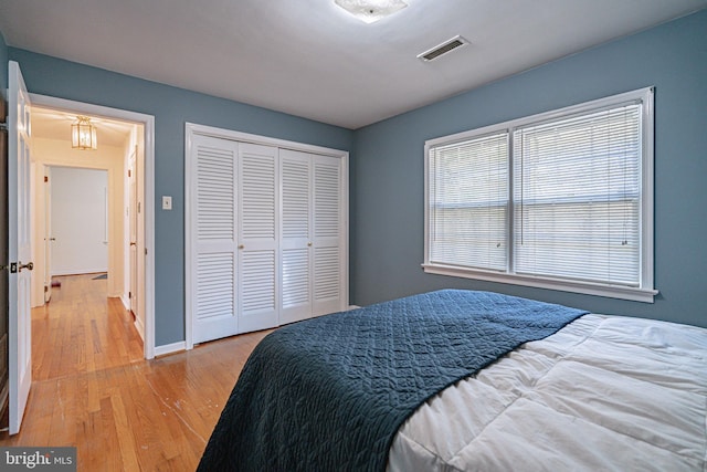 bedroom with baseboards, a closet, wood finished floors, and visible vents