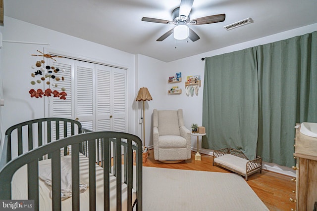 bedroom with a ceiling fan, visible vents, wood finished floors, and a closet