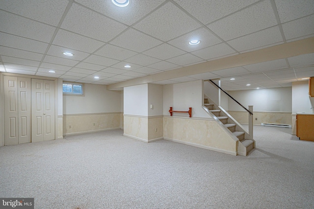 below grade area with carpet, a baseboard heating unit, wainscoting, and a drop ceiling
