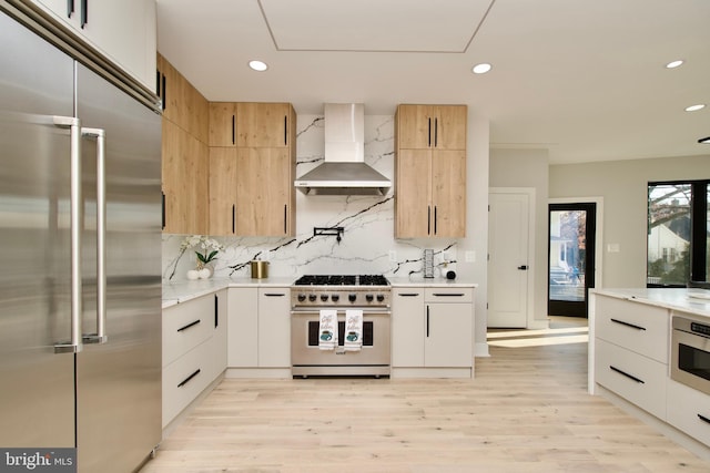 kitchen featuring light wood-style floors, tasteful backsplash, wall chimney range hood, and premium appliances