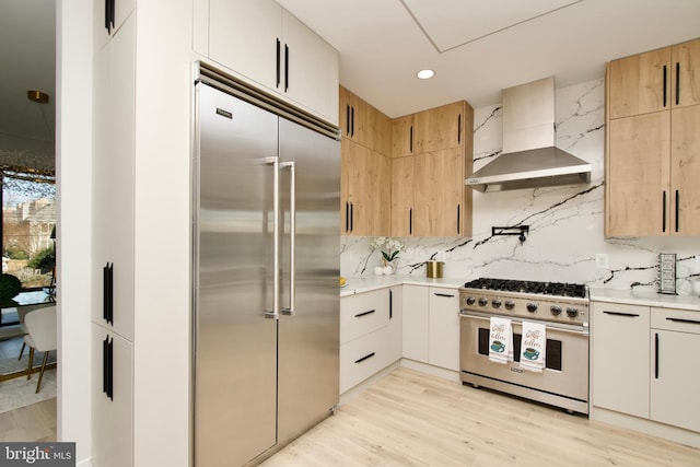 kitchen featuring wall chimney range hood, light countertops, backsplash, and high quality appliances