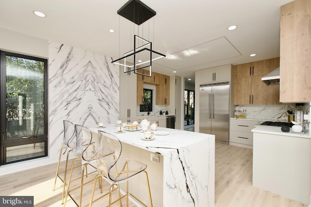 kitchen featuring light stone counters, a kitchen breakfast bar, stainless steel appliances, recessed lighting, and under cabinet range hood